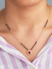 Gold necklace with a red gemstone pendant on a person wearing a purple and white striped shirt.