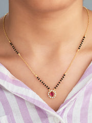 Gold necklace with a red gemstone pendant on a person wearing a purple and white striped shirt.