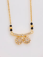 Gold necklace with black beads and floral pendants on a light gray background