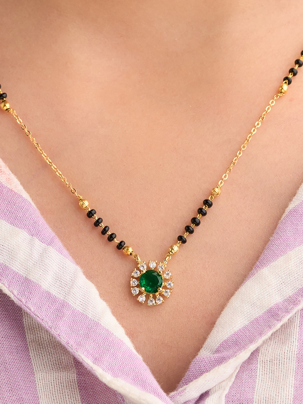 Gold necklace with a green gemstone on a person wearing a light purple and white striped garment.