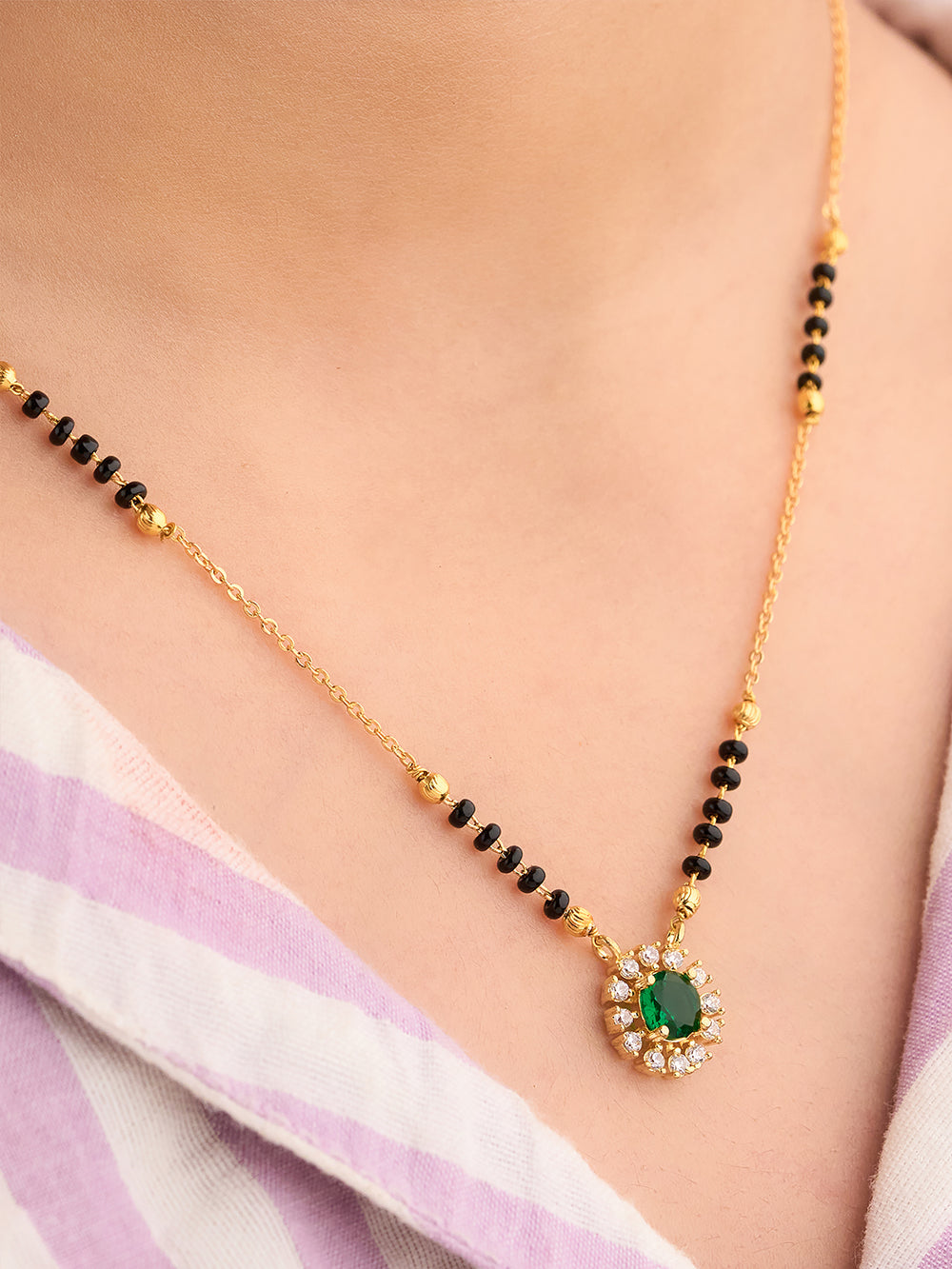 Gold necklace with green gemstone pendant on a person wearing a light purple saree.