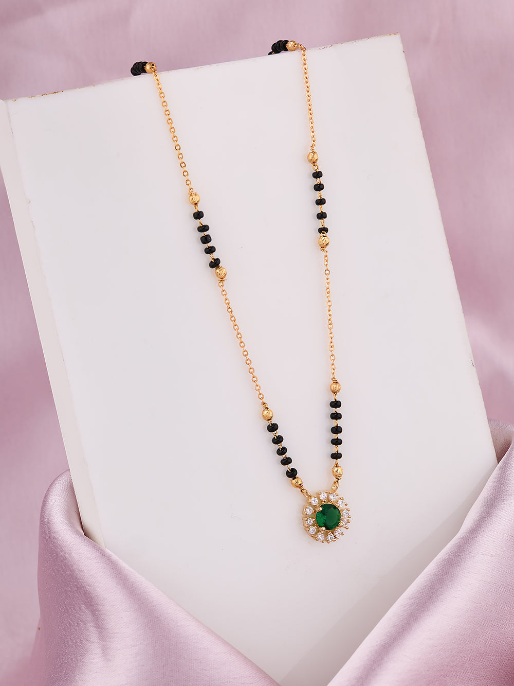 Necklace with green gemstone and black beads on a white stand against a pink background