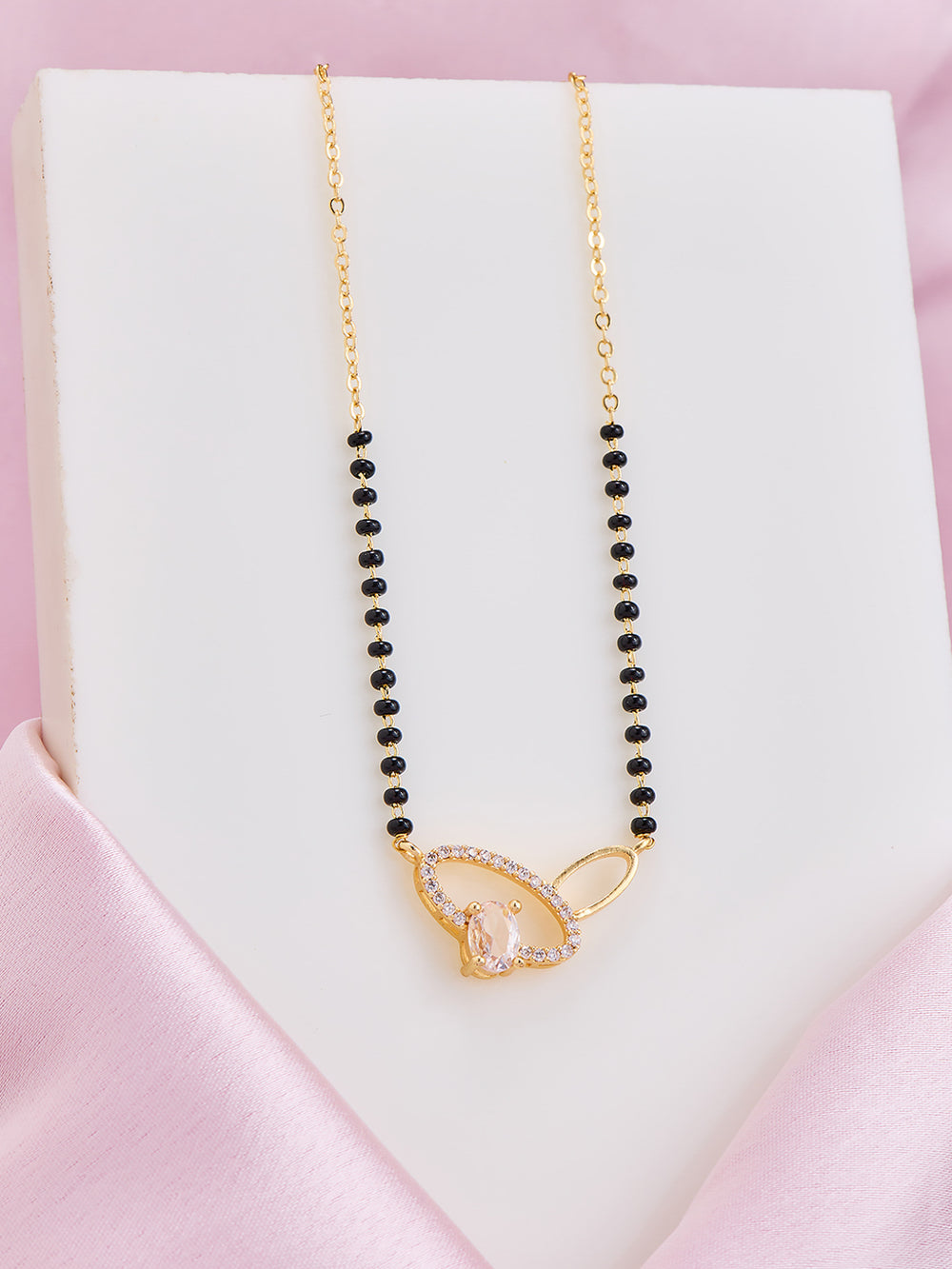 Necklace with black beads and gold clasp on a pink satin surface