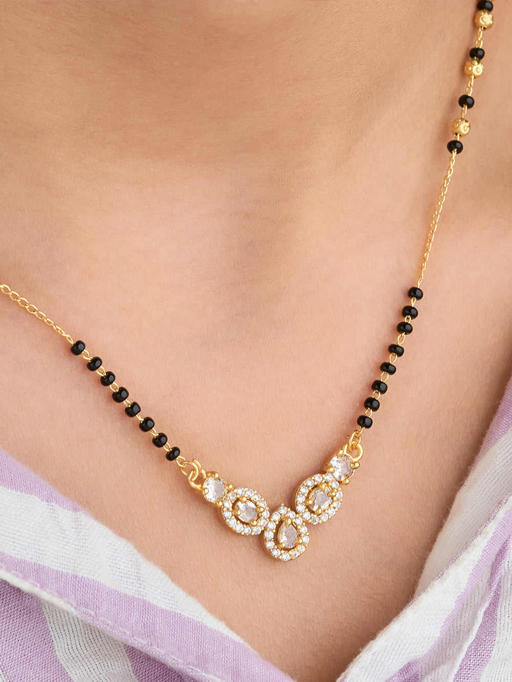 Gold necklace with black beads and white stones on a person wearing a light purple garment.