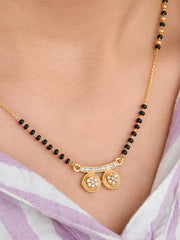 Gold necklace with black beads and circular pendants on a person wearing a light purple garment.
