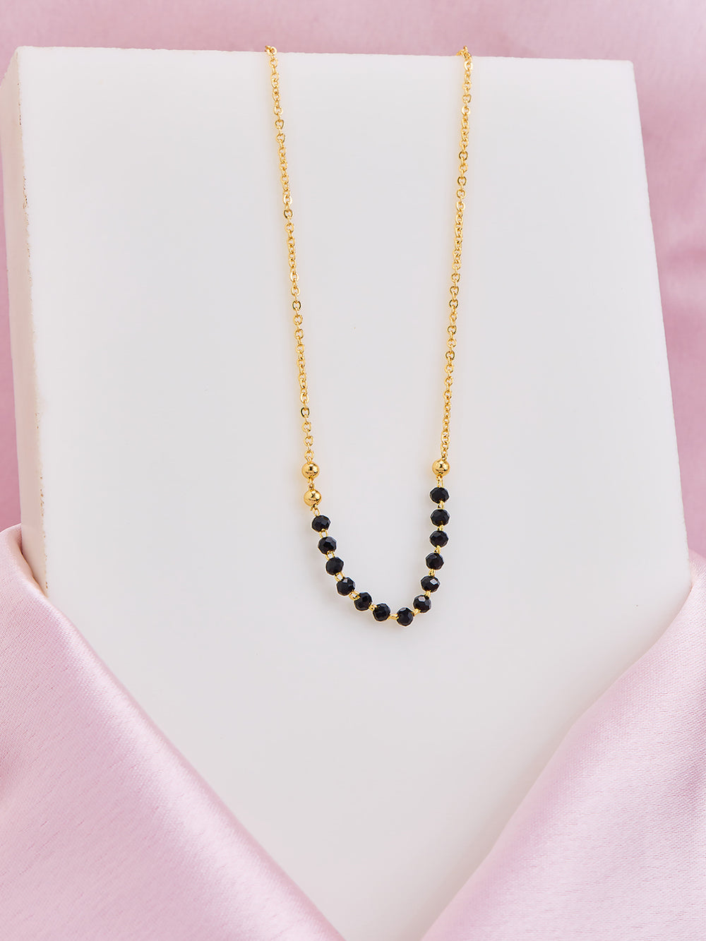 Gold necklace with black beads on a white card with pink border