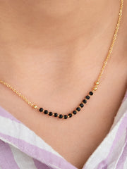 Gold necklace with black beads worn by a person, with a blurred background