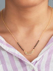 Gold necklace with black beads worn by a person in a light purple and white striped shirt.