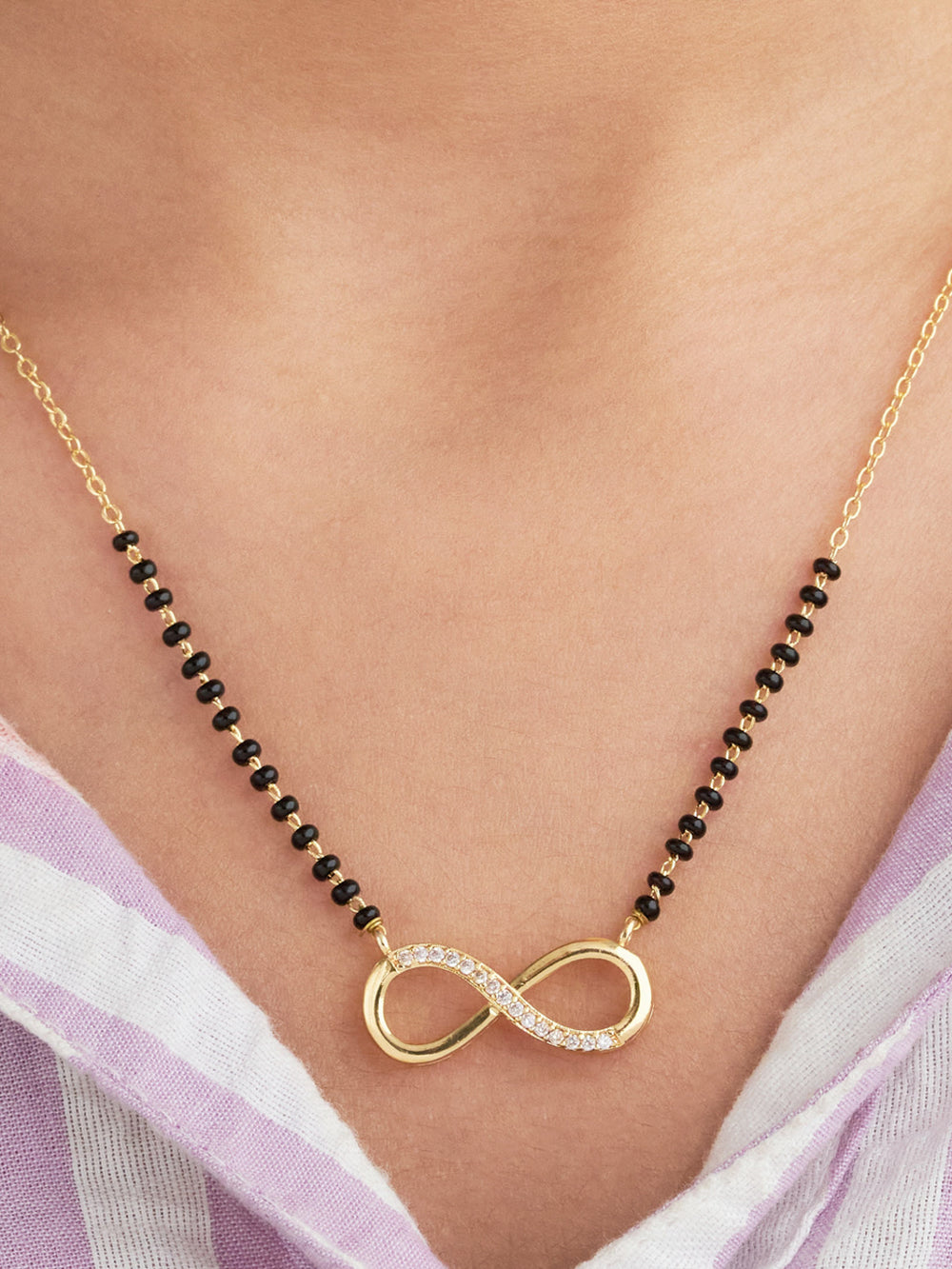 Gold necklace with an infinity symbol pendant on a person wearing a light purple garment.