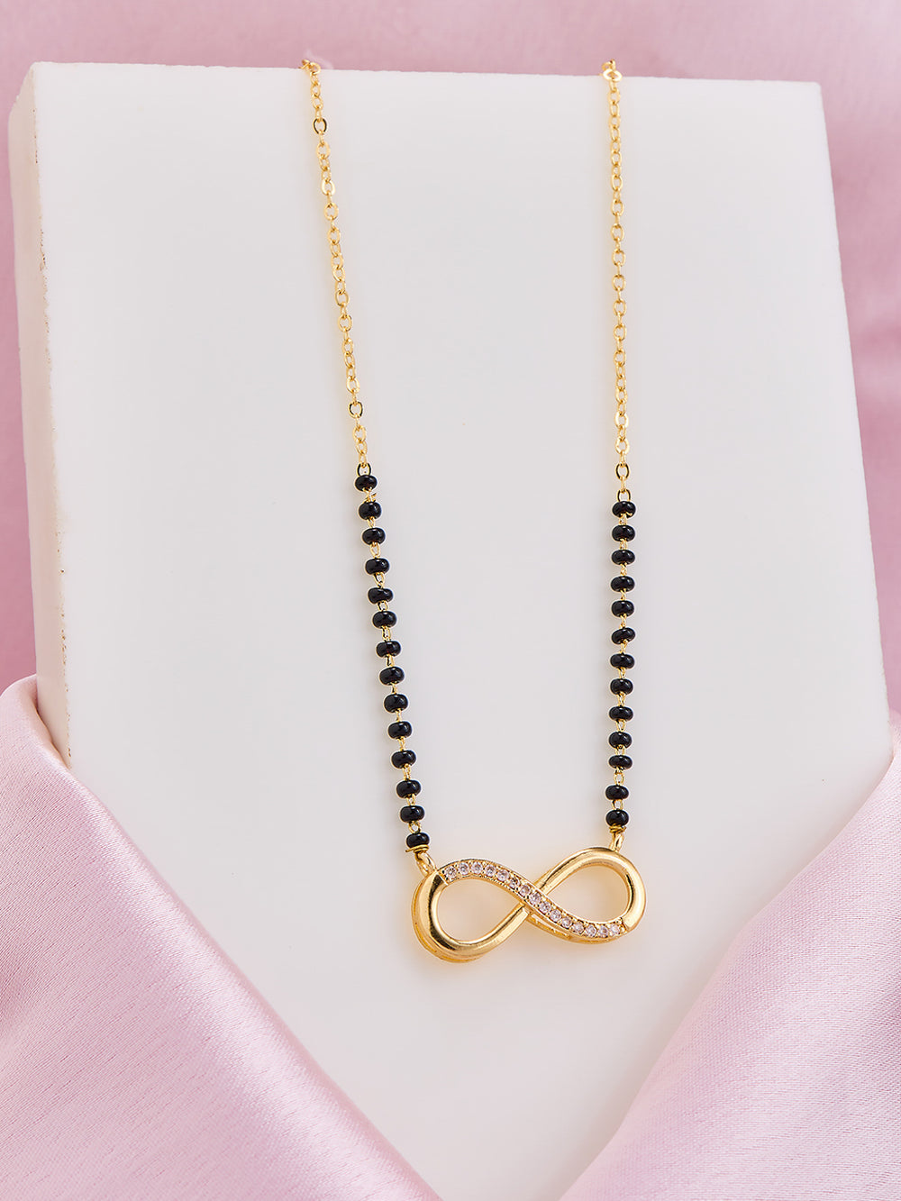 Necklace with black beads and gold infinity pendant on a pink satin surface