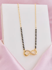 Necklace with black beads and gold infinity pendant on a pink satin surface