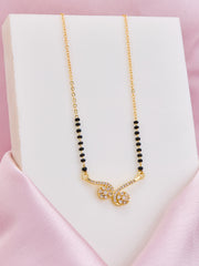 Gold necklace with black beads on a white stand against a pink background