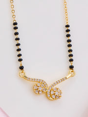 Gold necklace with black beads and a decorative clasp on a light pink background