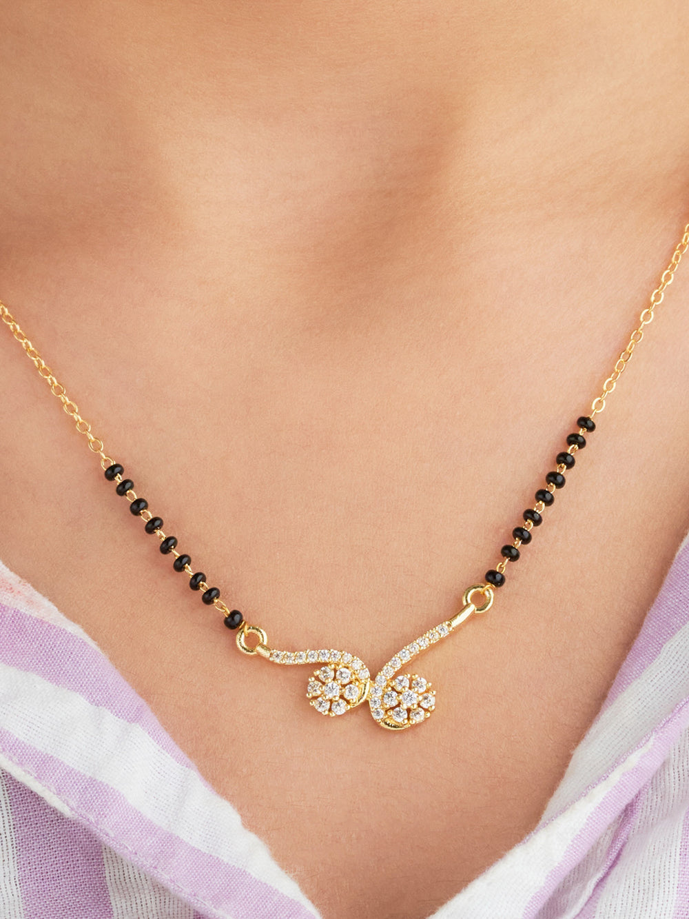 Gold necklace with black beads and floral pendants on a person wearing a light purple top.