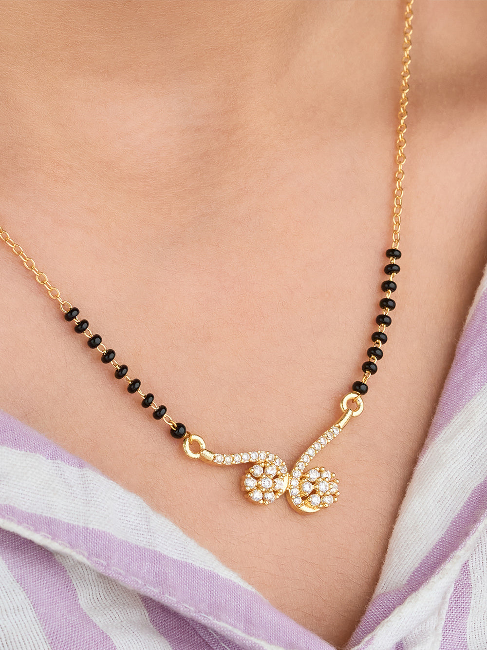 Gold necklace with black beads and a floral pendant on a person wearing a light purple scarf.