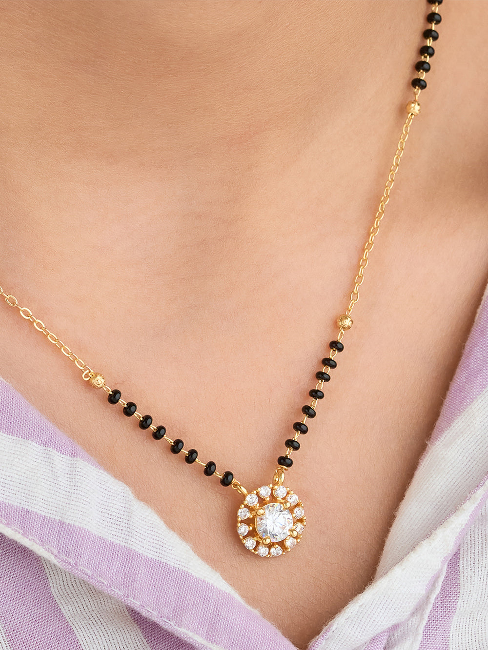 Necklace with black beads and a gold chain on a person wearing a light purple garment.