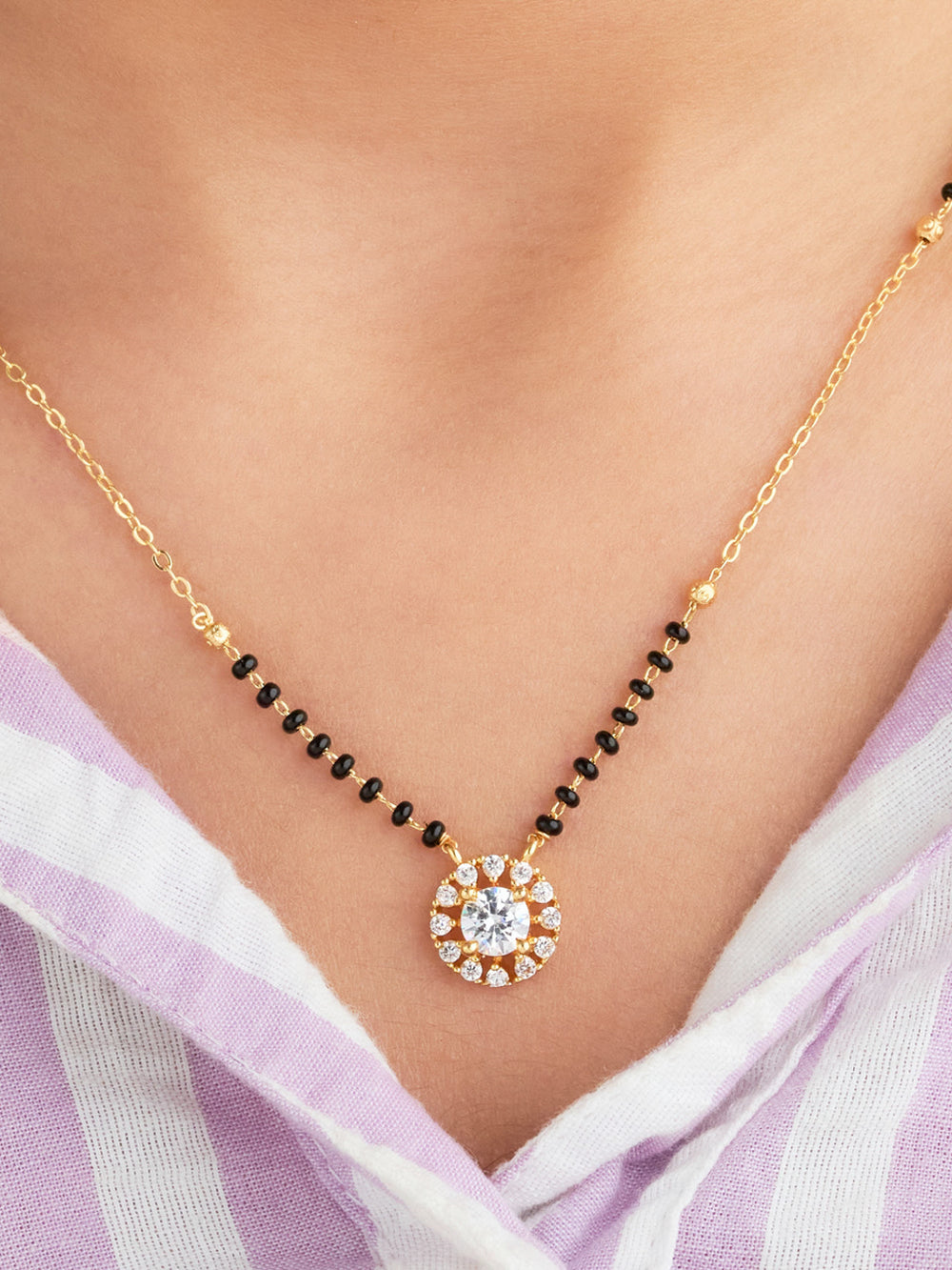 Gold necklace with a round pendant on a person wearing a light purple scarf.