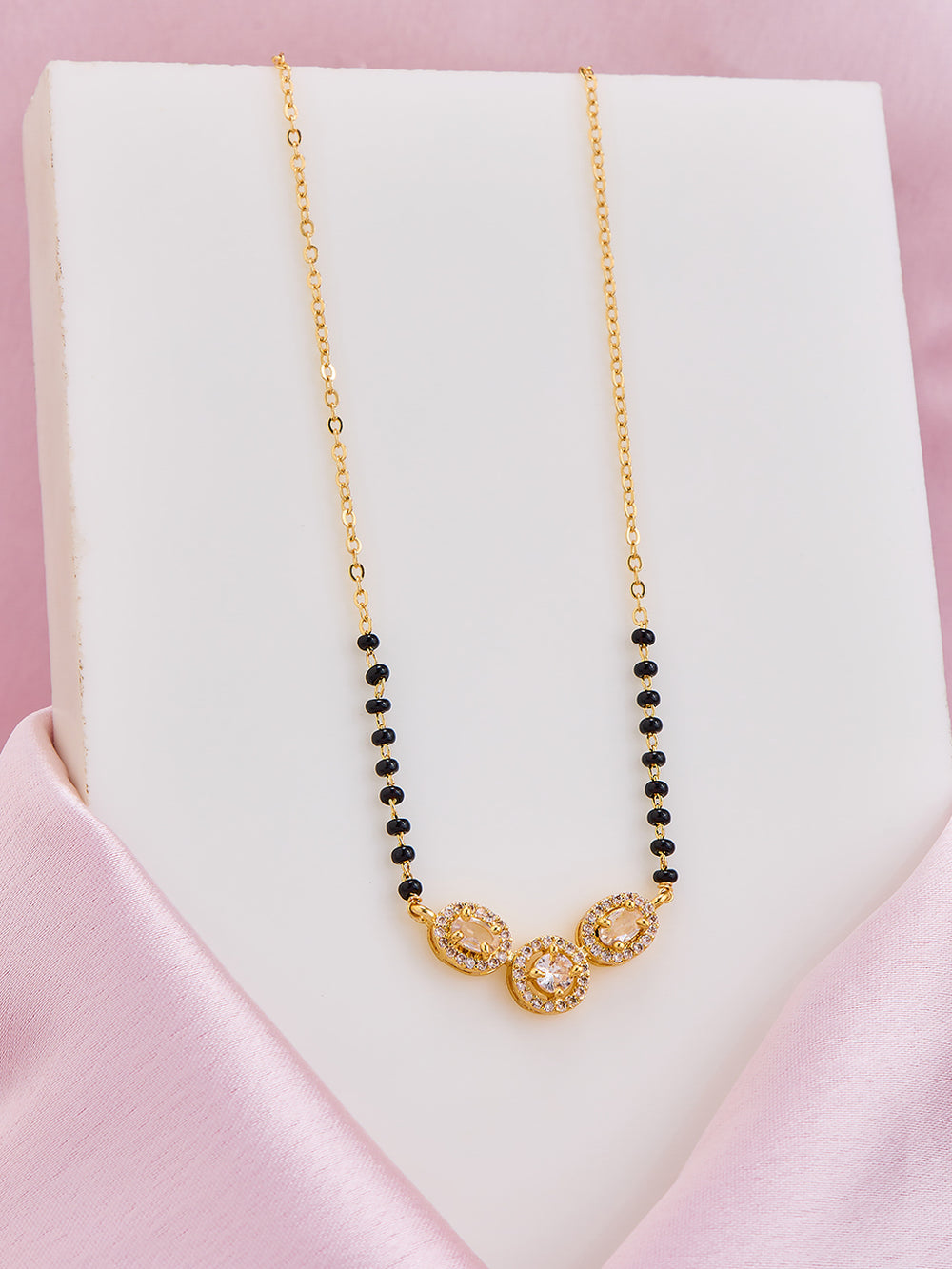 Gold necklace with black beads on a white stand against a pink background