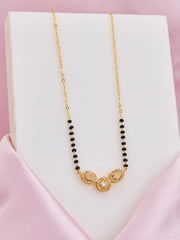 Gold necklace with black beads on a white stand against a pink background