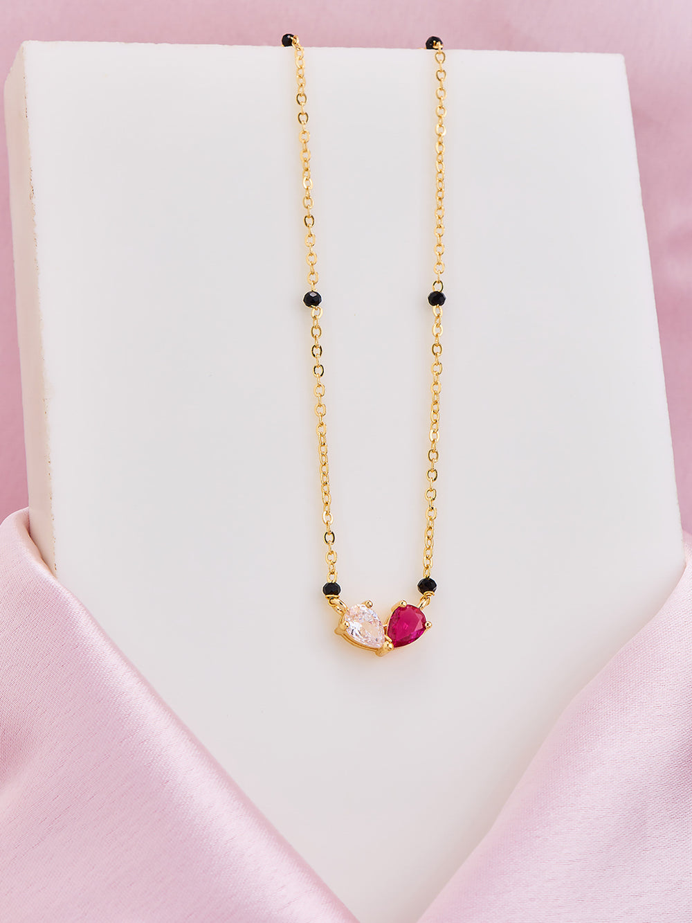 Gold necklace with a heart-shaped pink pendant on a white stand with a pink background