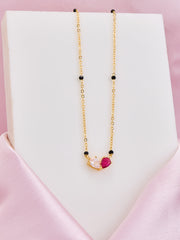 Gold necklace with a heart-shaped pink pendant on a white stand with a pink background