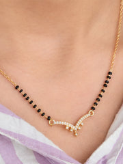 Gold necklace with black beads on a person wearing a light purple garment.