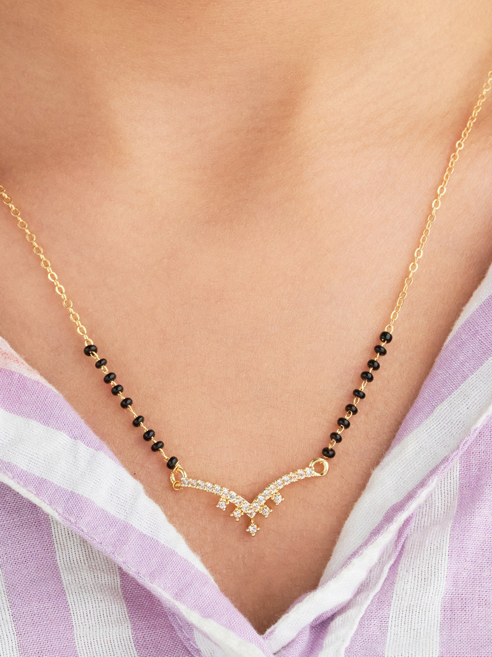 Gold necklace with black beads on a person wearing a light purple and white striped garment.