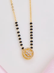 Necklace with black beads and a gold pendant on a light pink background
