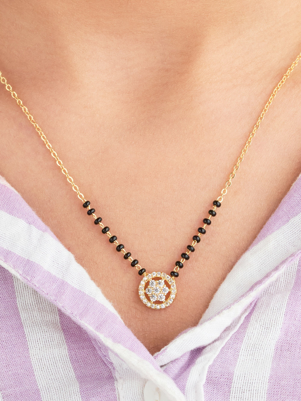 Gold necklace with black beads and a circular pendant on a person wearing a light purple top.