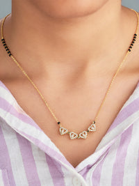 Gold necklace with heart-shaped gemstones worn by a person in a striped shirt.