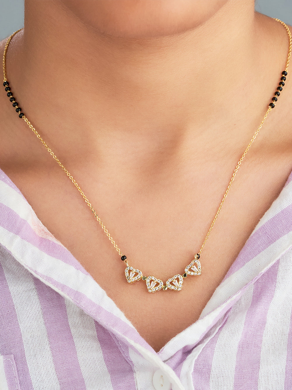 Gold necklace with heart-shaped gemstones worn by a person in a striped shirt.