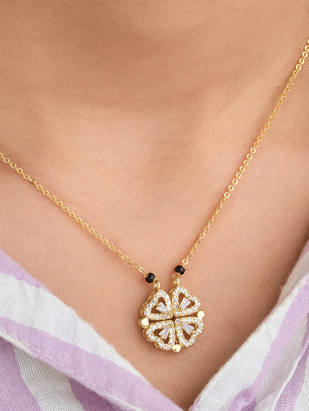 Gold necklace with a decorative pendant on a person wearing a light purple top.