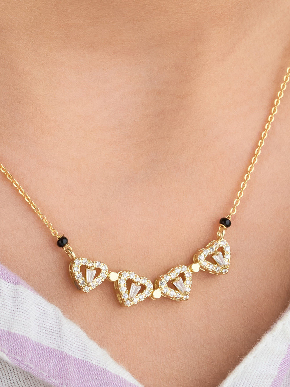 Gold necklace with heart-shaped pendants on a person wearing a striped garment.