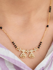 Gold necklace with black beads on a person wearing a light purple garment.