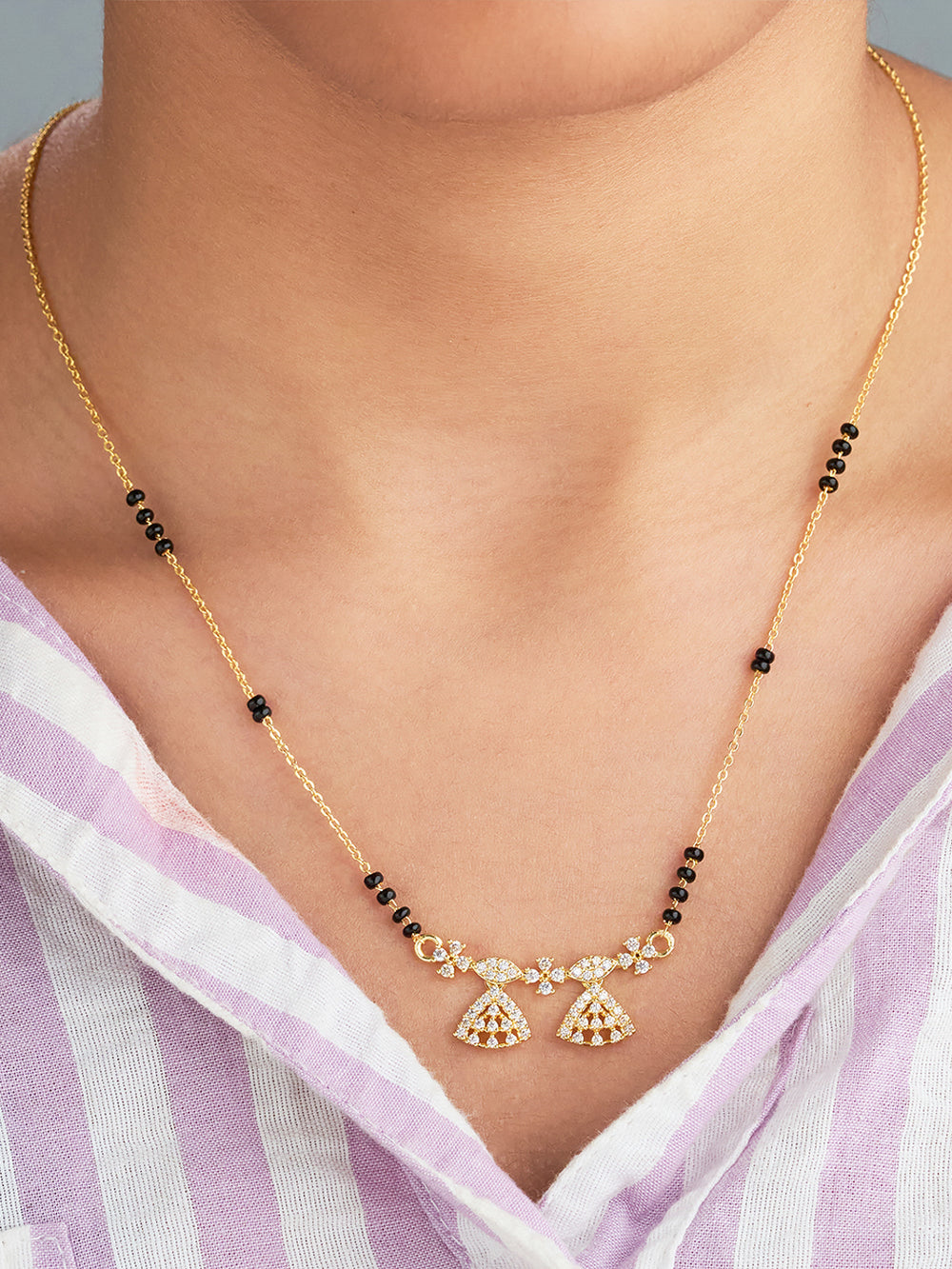 Gold necklace with black beads and decorative elements on a person wearing a light purple and white striped garment.