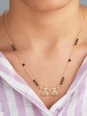 Gold necklace with black beads and decorative elements on a person wearing a light purple and white striped garment.