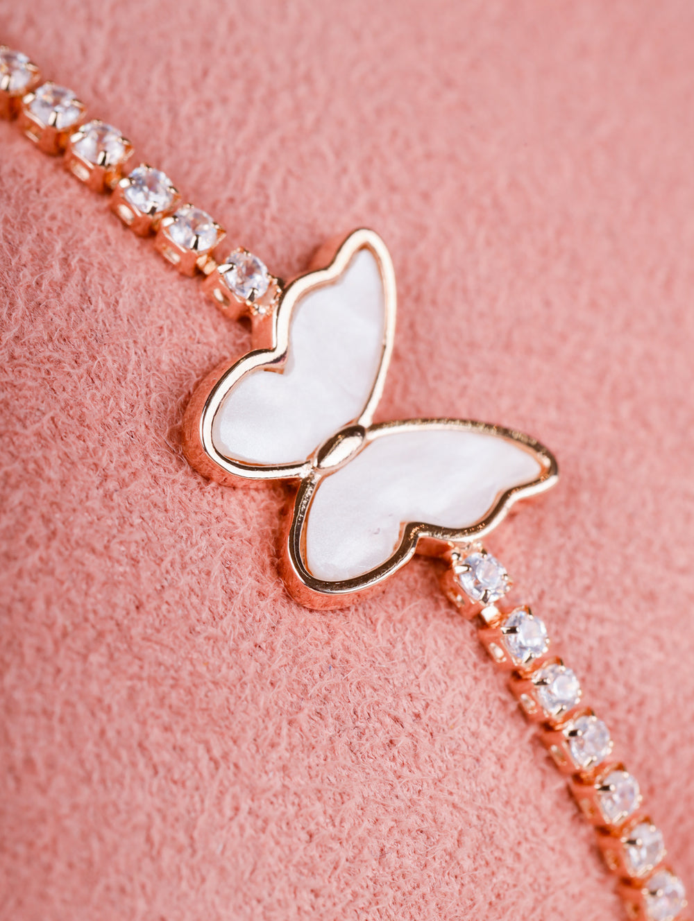 Butterfly-shaped bracelet with rose gold and clear gemstones on a pink background