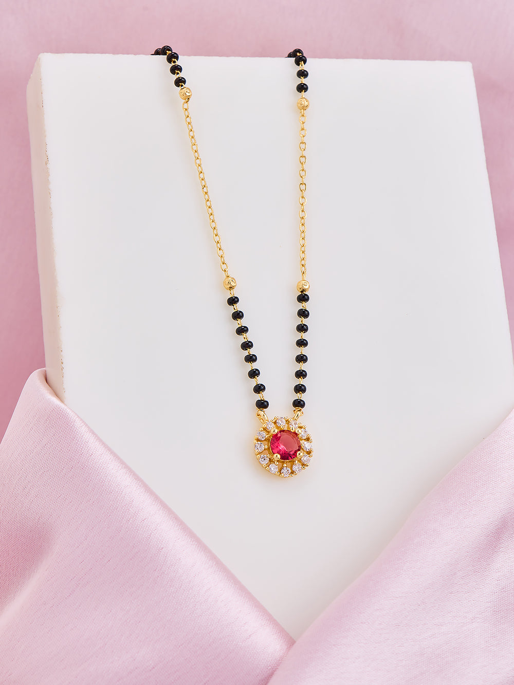 Necklace with black beads and a colorful pendant on a pink satin surface