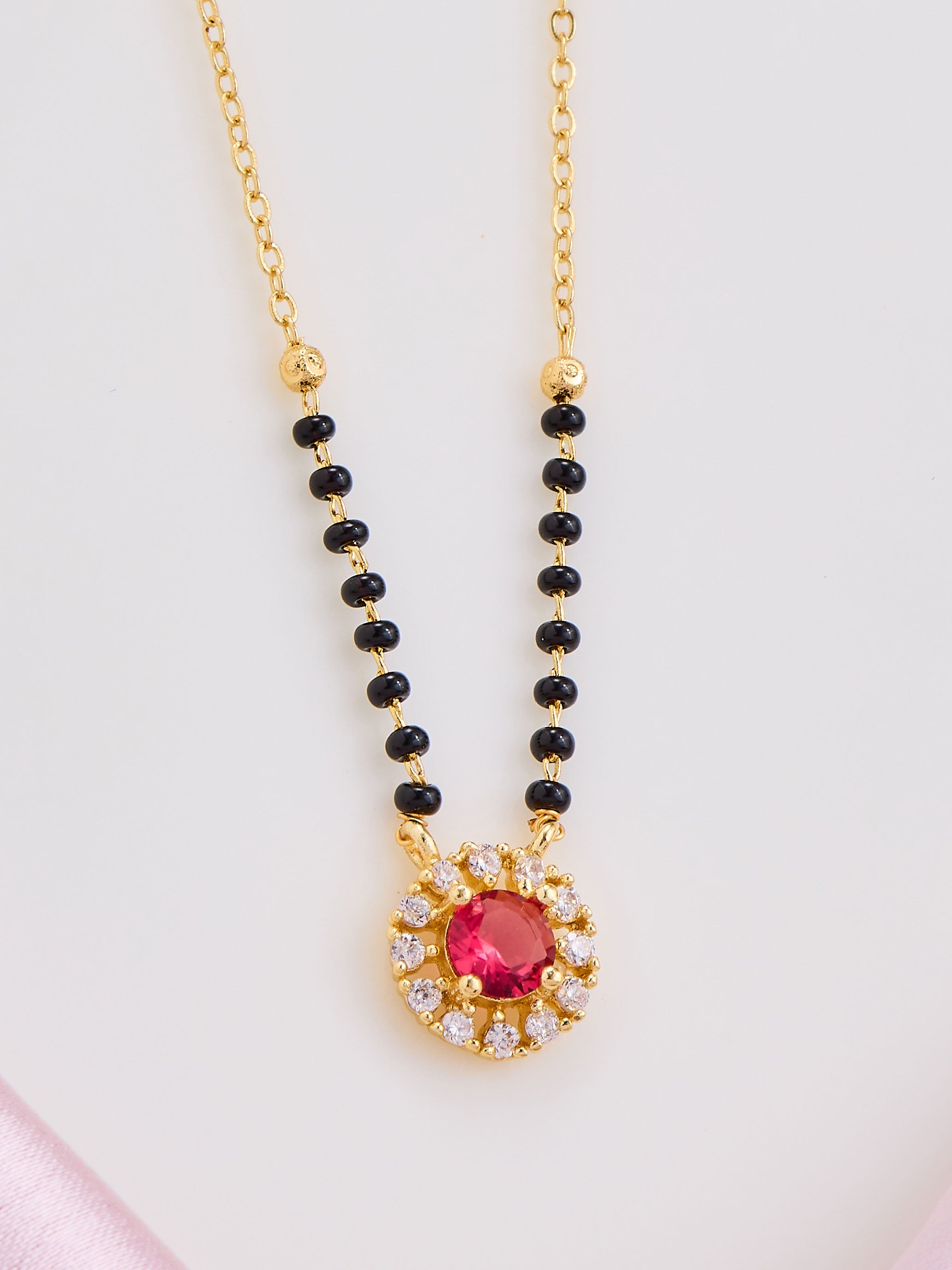 Necklace with black beads and a red gemstone pendant on a light pink background