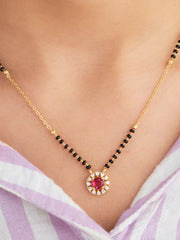Necklace with a red gemstone and gold chain on a person wearing a purple top.
