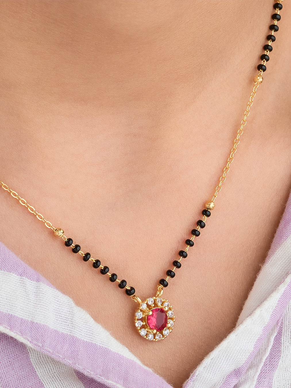 Gold necklace with a red gemstone pendant on a person wearing a light purple saree.