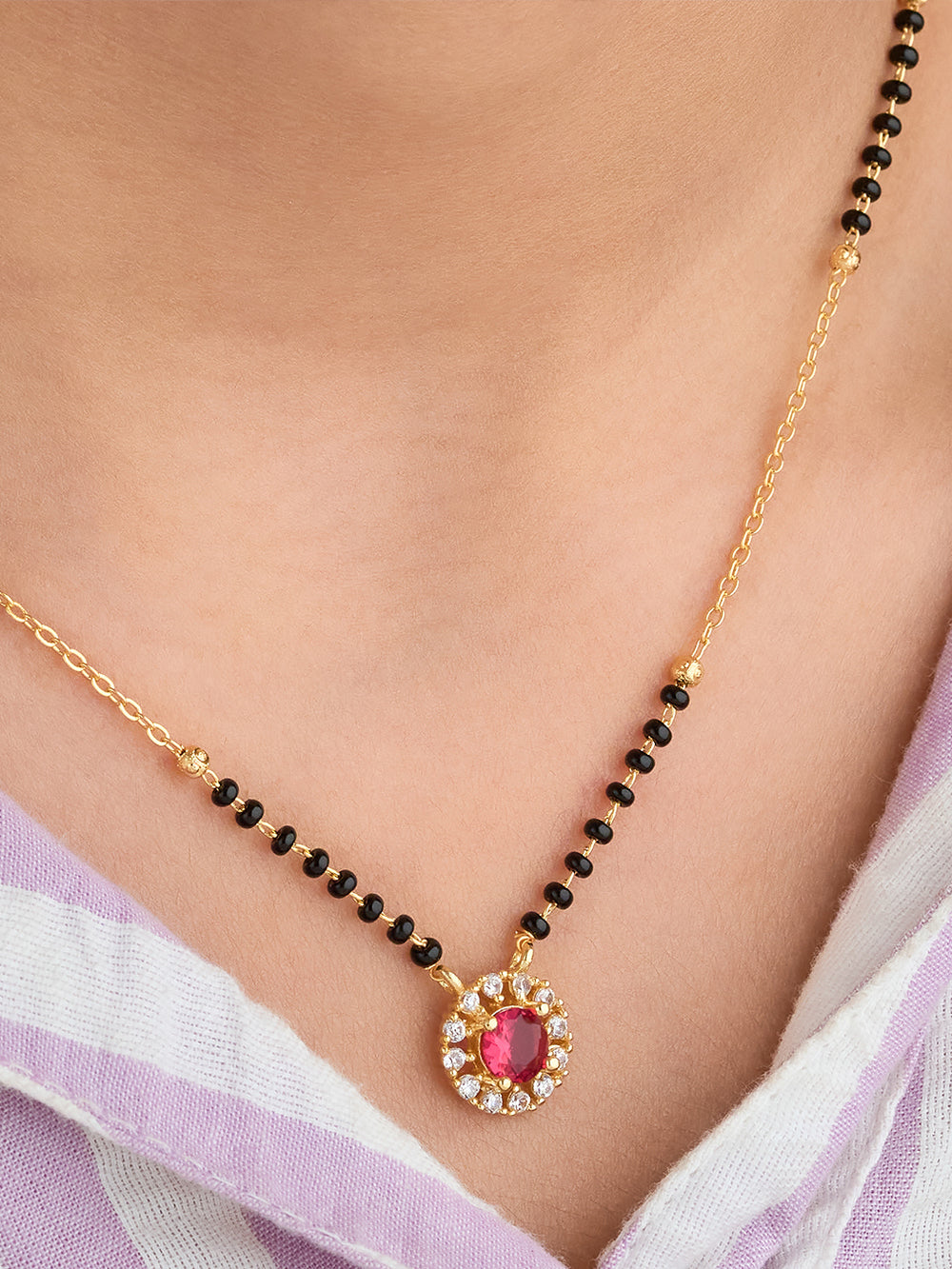 Gold necklace with a red gemstone pendant on a person wearing a light purple saree.