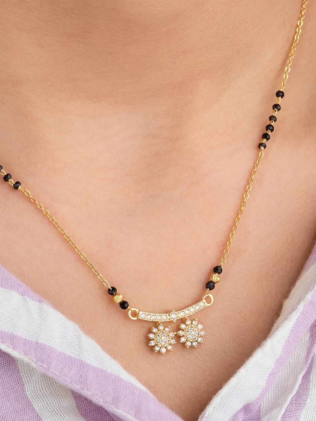 Gold necklace with black beads and floral pendants on a person wearing a light purple garment.