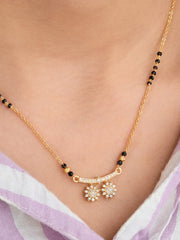 Gold necklace with black beads and floral pendants on a person wearing a light purple garment.