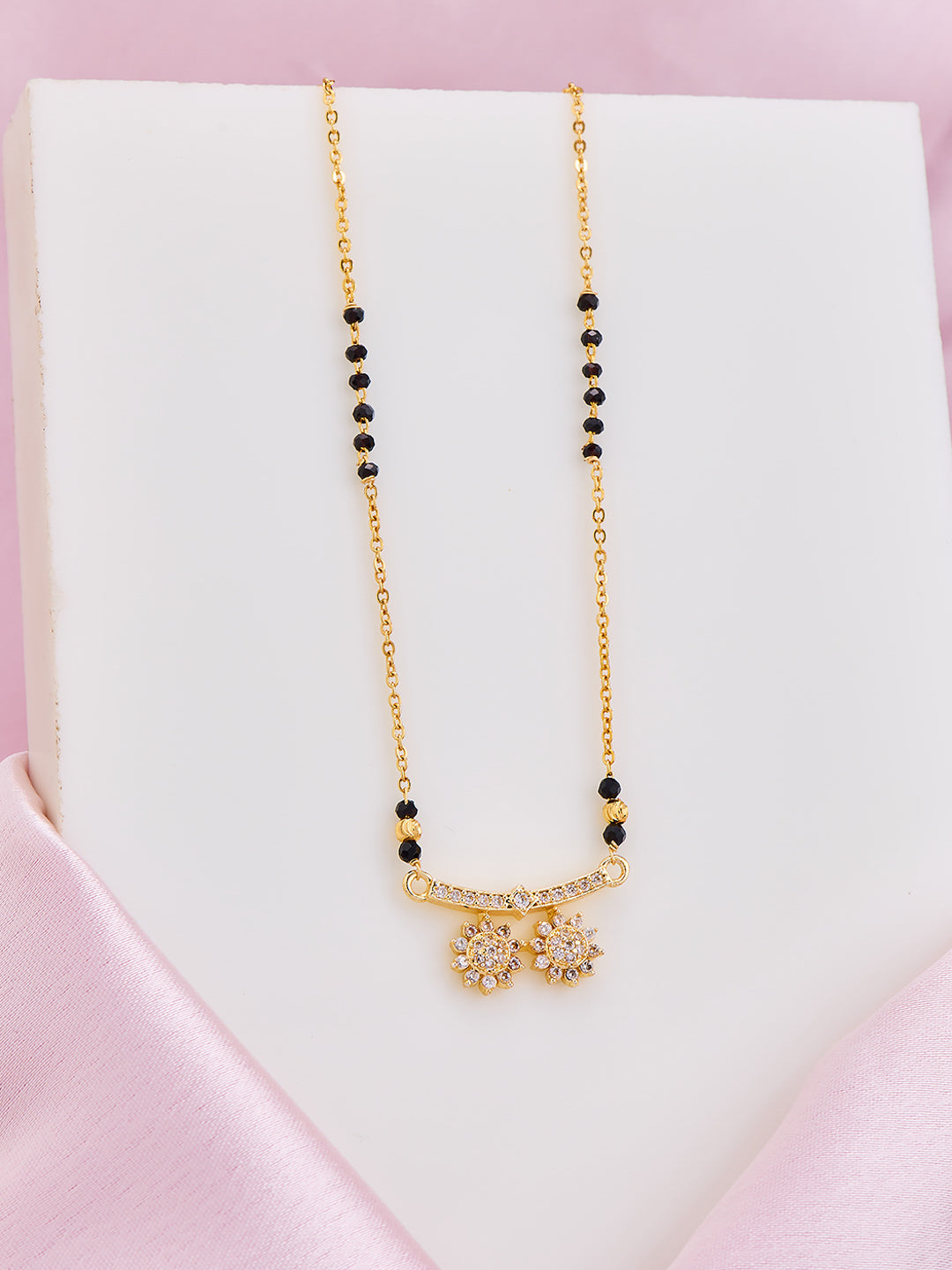 Gold necklace with black beads on a white box with pink satin border