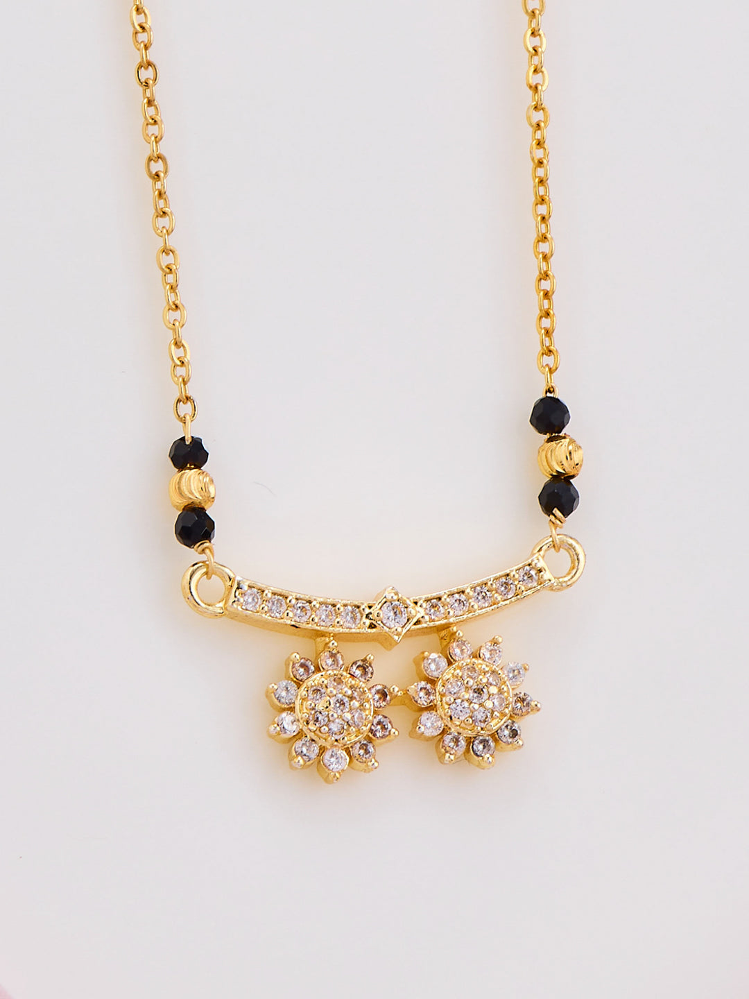 Gold necklace with black beads and floral pendants on a light gray background