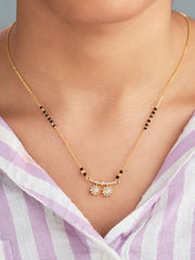 Gold necklace with black beads and floral pendants on a person wearing a striped shirt.