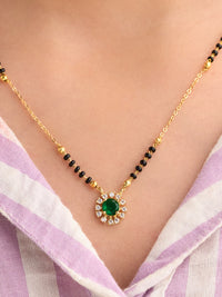 Gold necklace with a green gemstone on a person wearing a light purple and white striped garment.