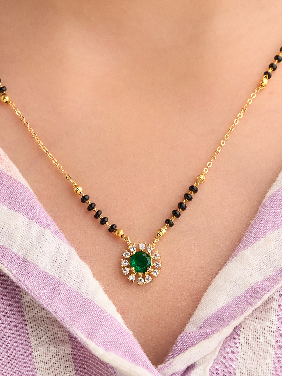 Gold necklace with a green gemstone on a person wearing a light purple and white striped garment.