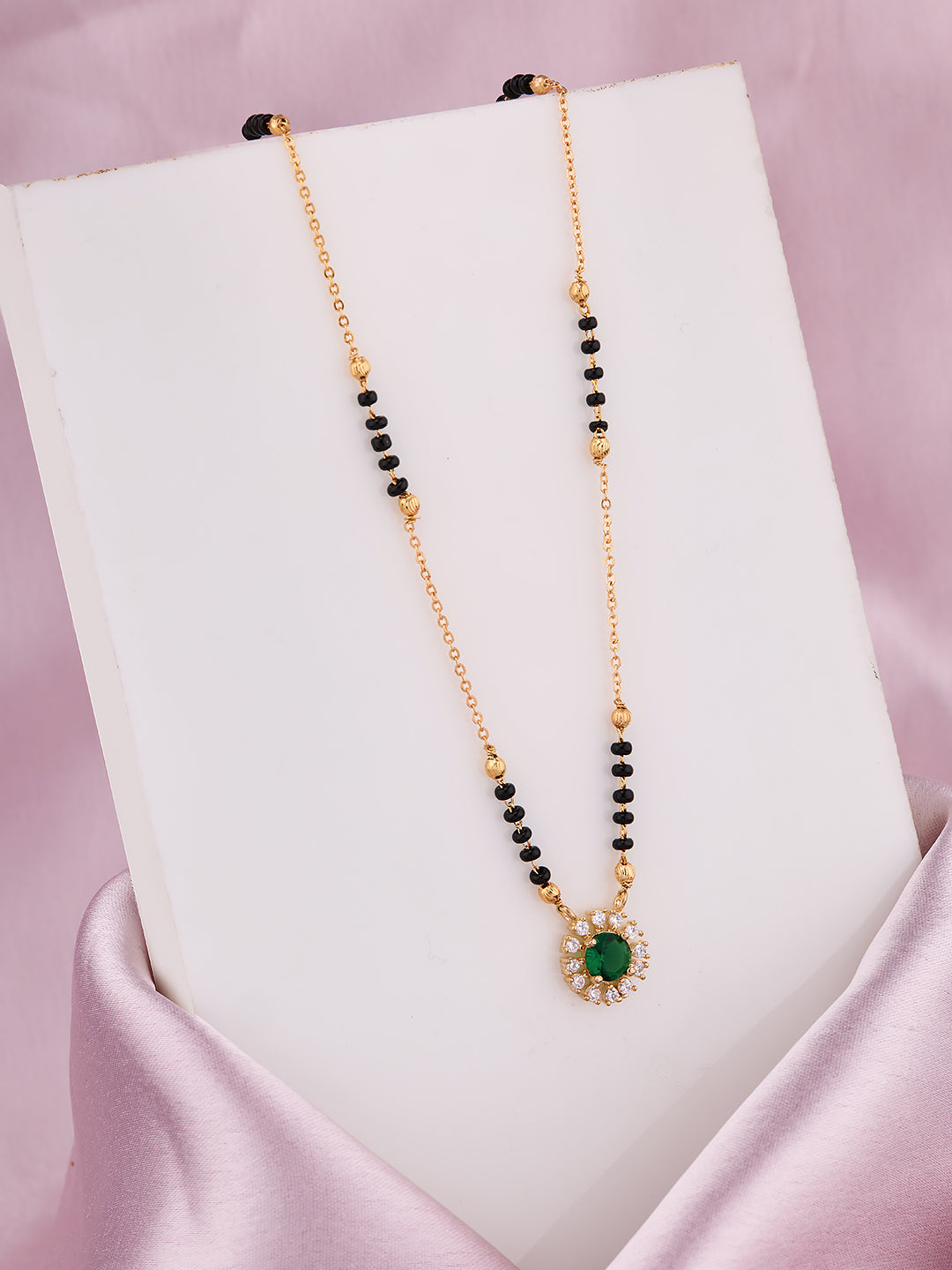 Necklace with green gemstone and black beads on a white stand against a pink background